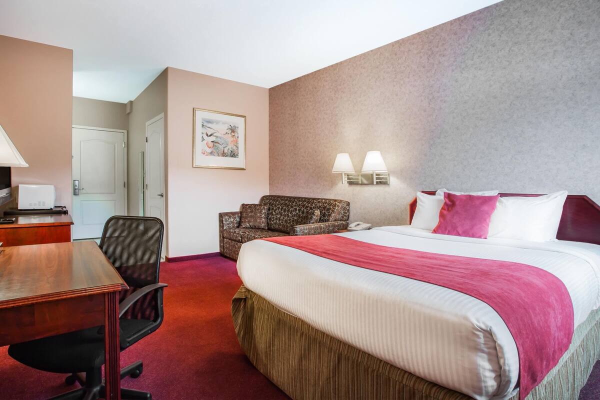 Ein Hotelzimmer mit einem großen Bett, einem Schreibtisch mit Lampe, einem Sessel und einem Bild an der Wand.