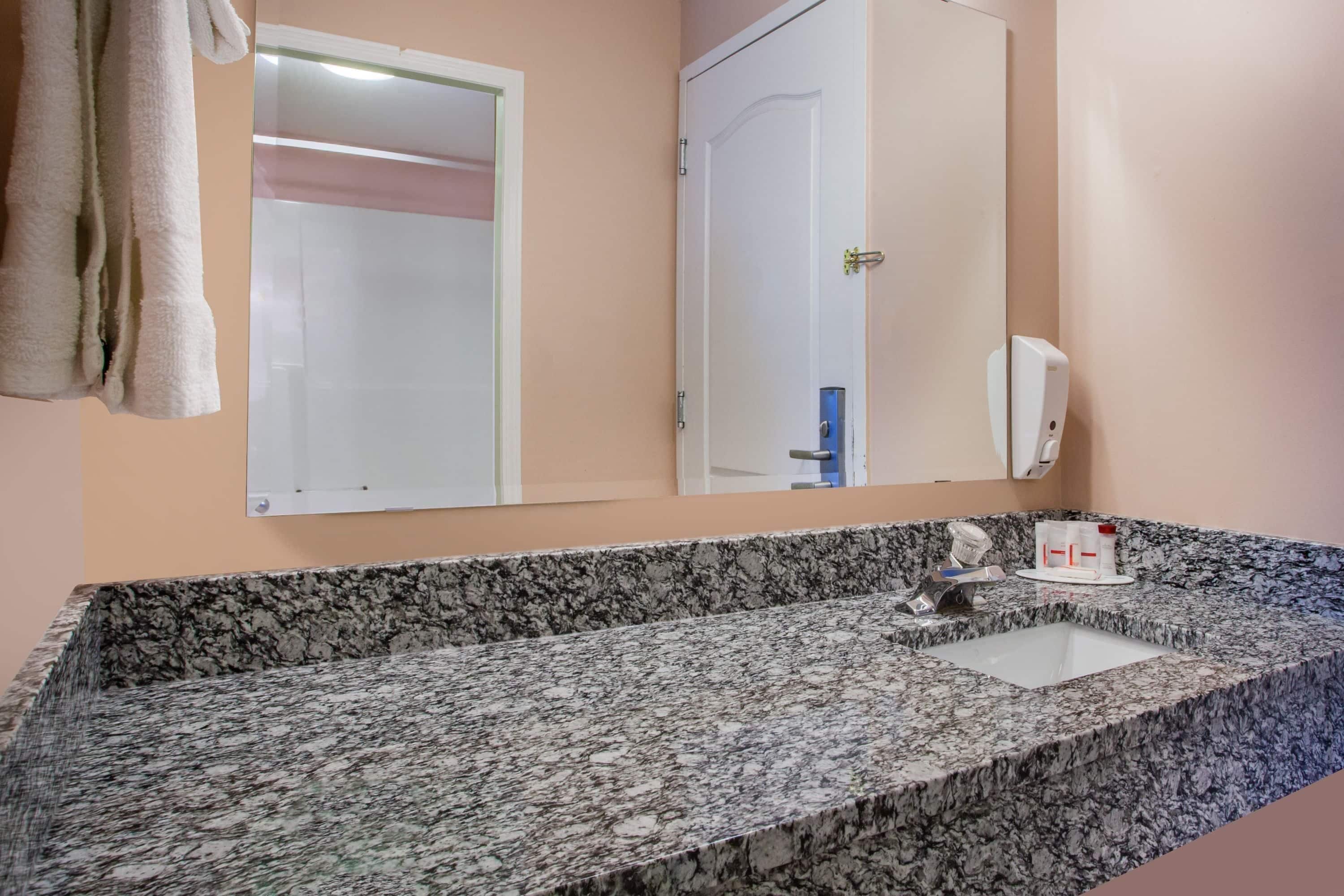 A bathroom with a granite countertop, a sink, a mirror, a towel rack, and a door.