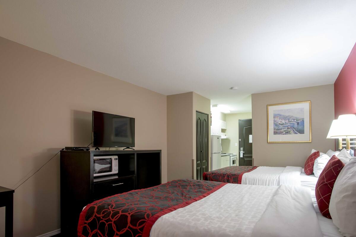 Ein Hotelzimmer mit zwei Betten, einem Fernseher, einer Mikrowelle und einem gerahmten Bild an der Wand.