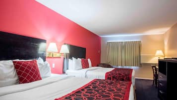 A hotel room with two beds, red and white bedding, a TV, a desk, and a chair.