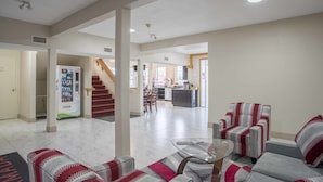 Uma sala de estar espaçosa com uma mesa de centro de vidro, poltronas listradas e uma escada que leva a uma cozinha.