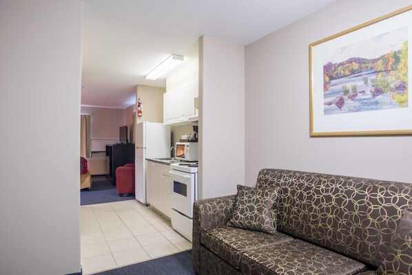 A compact living space with a kitchenette, a sofa, and a framed landscape painting. - Ramada by Wyndham 100 Mile House (100 Mile House)