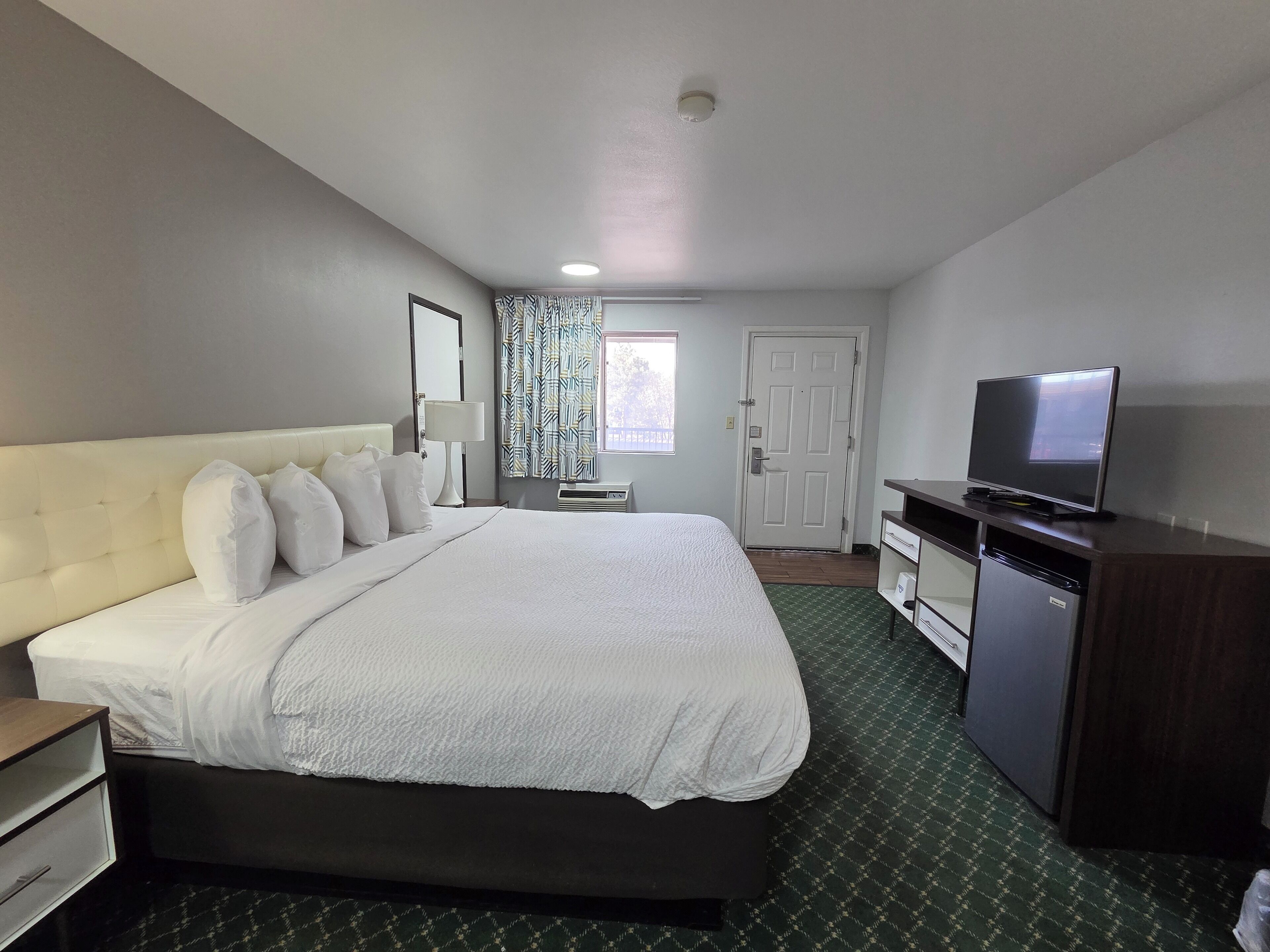A hotel room with a large bed, a television, a desk, and a wardrobe.