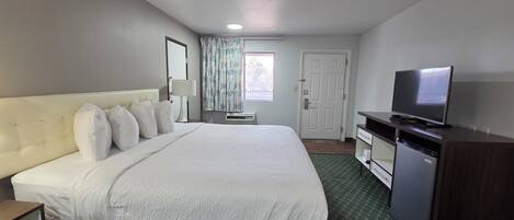 A hotel room with a large bed, a television, a desk, and a wardrobe.