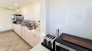 A modern kitchen with a stainless steel refrigerator, a coffee machine, a toaster, and a wooden cutting board on the counter.