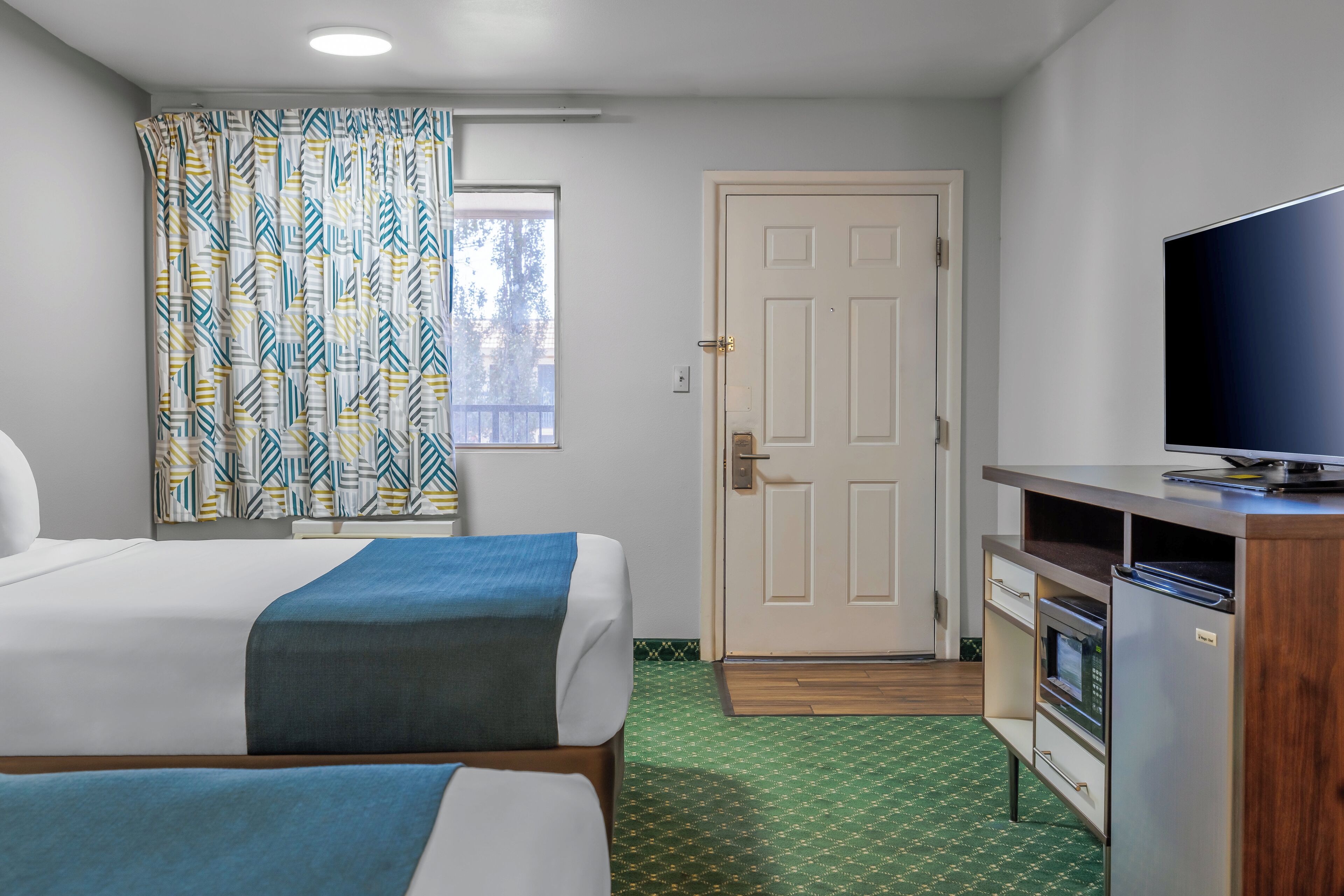 A hotel room with two beds, a television, a kitchenette, and a door.