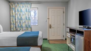 A hotel room with two beds, a television, a kitchenette, and a door.