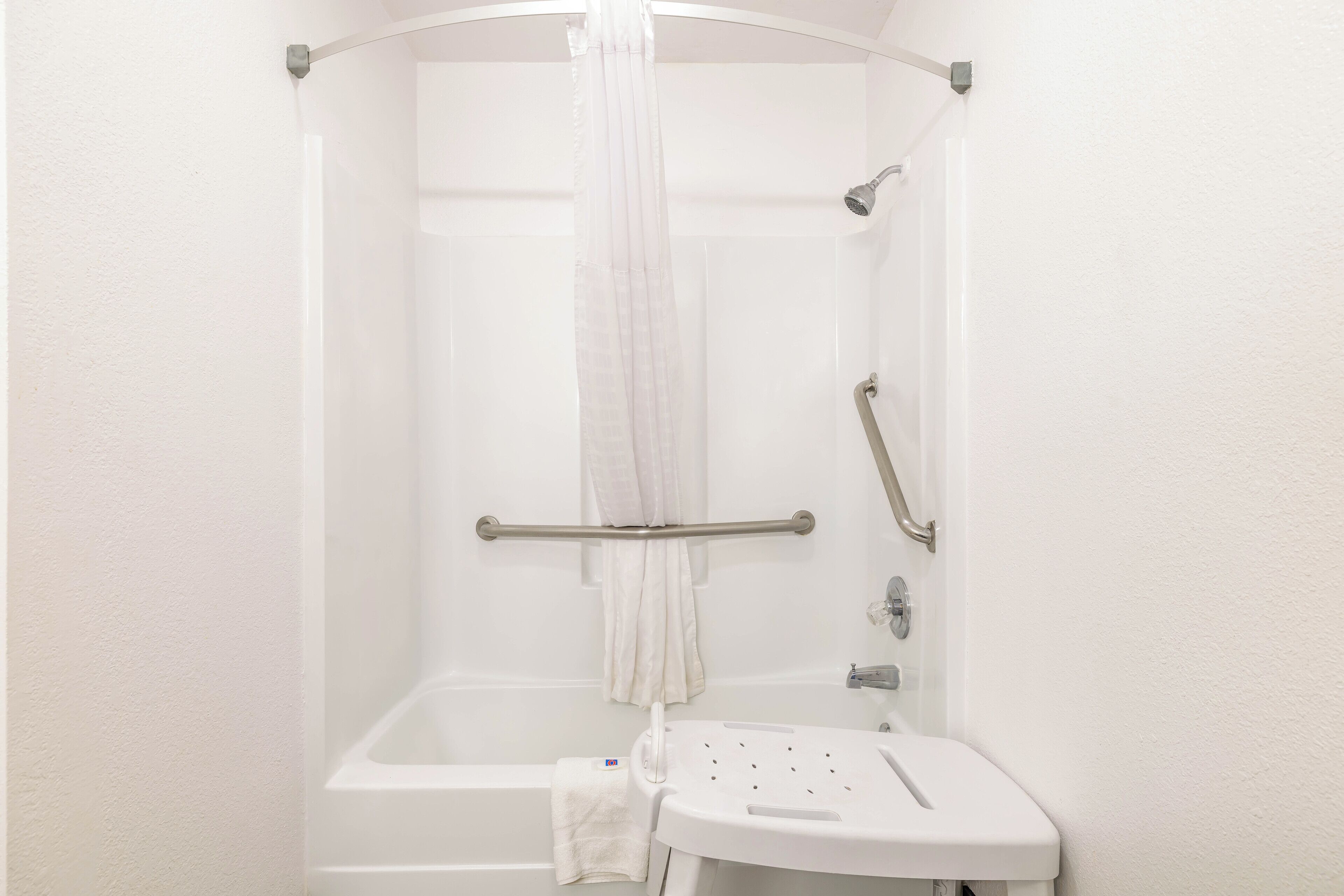 A white bathroom with a shower, a grab bar, a handheld showerhead, and a small sink with a handheld showerhead.