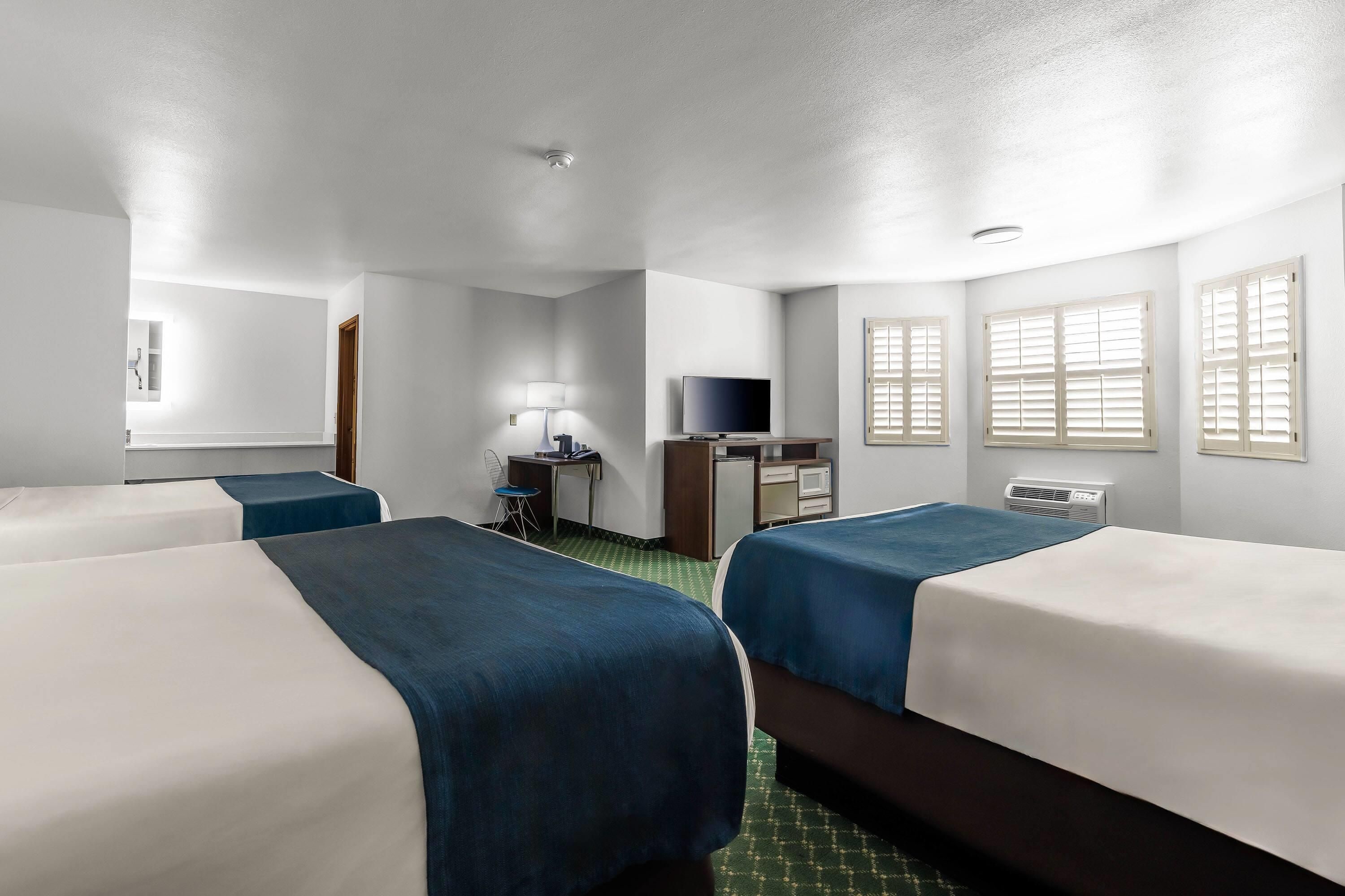 A hotel room with two beds, a desk with a television, a lamp, and a window with shutters.