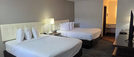 Quarto de hotel com duas camas, uma escrivaninha, televisão e uma luminária.