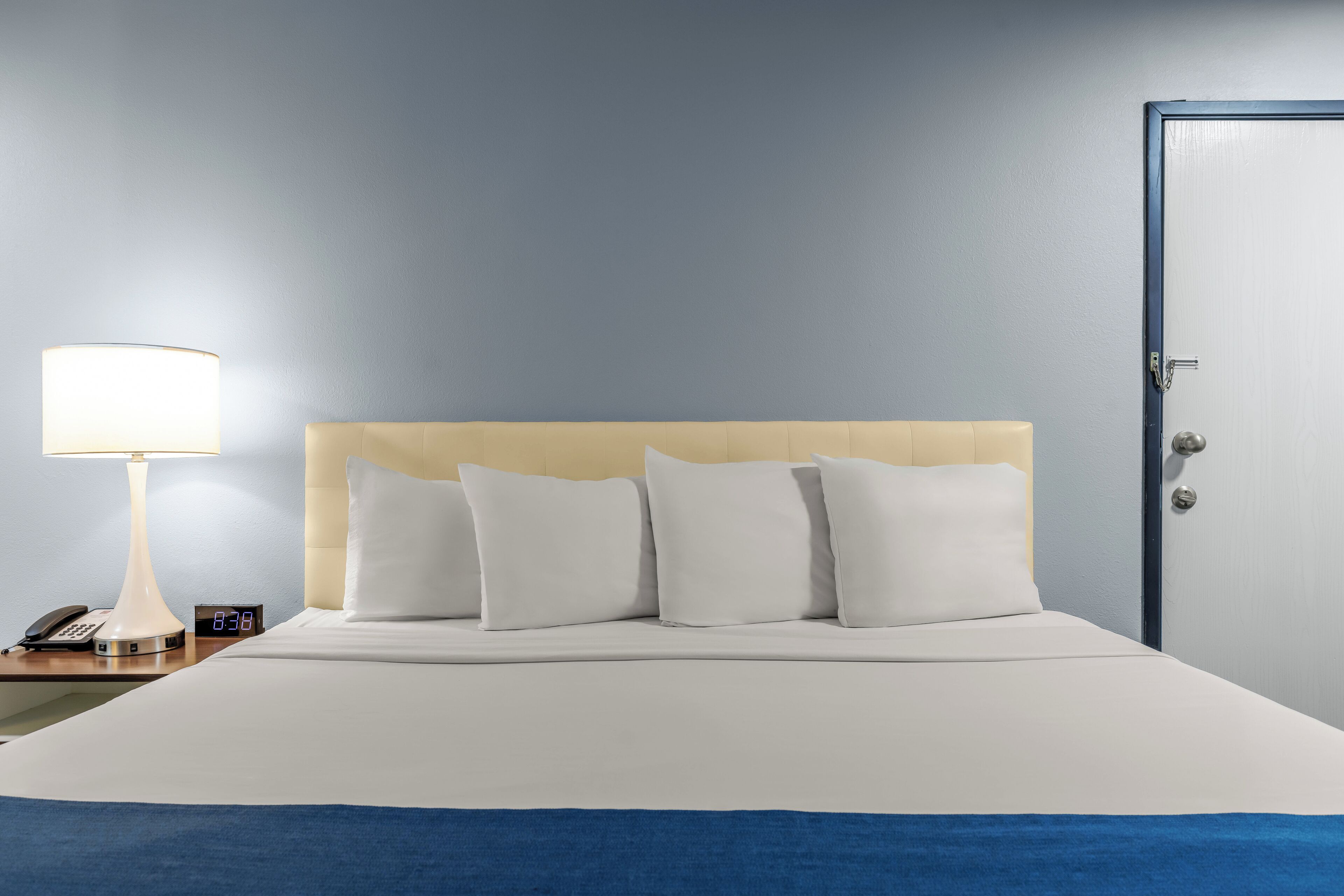 Une chambre d’hôtel avec un lit, une table de chevet avec une lampe, une horloge et une porte.