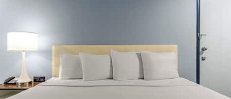 Una habitación de hotel con cama, mesita de noche con lámpara, un reloj y una puerta.