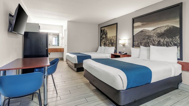 A hotel room with two beds, a desk, chairs, a TV, and artwork on the walls.