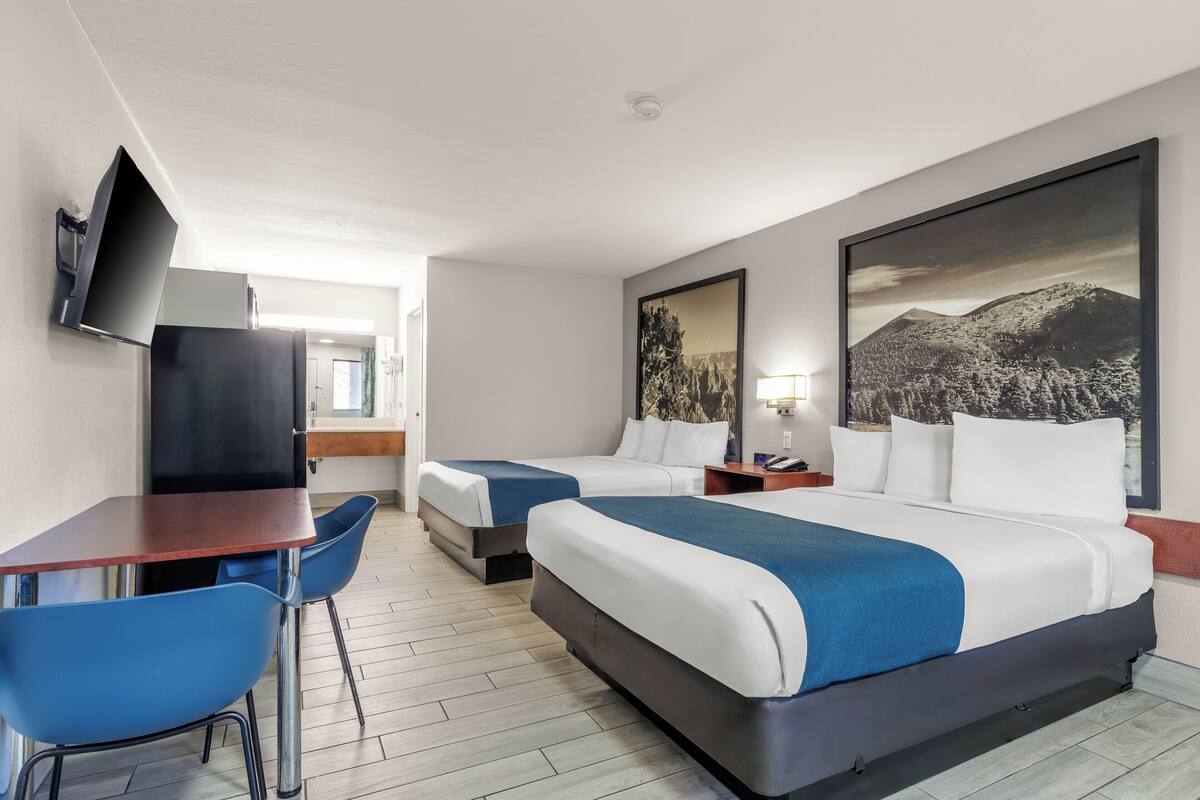 A hotel room with two beds, a desk, chairs, a TV, and artwork on the walls.