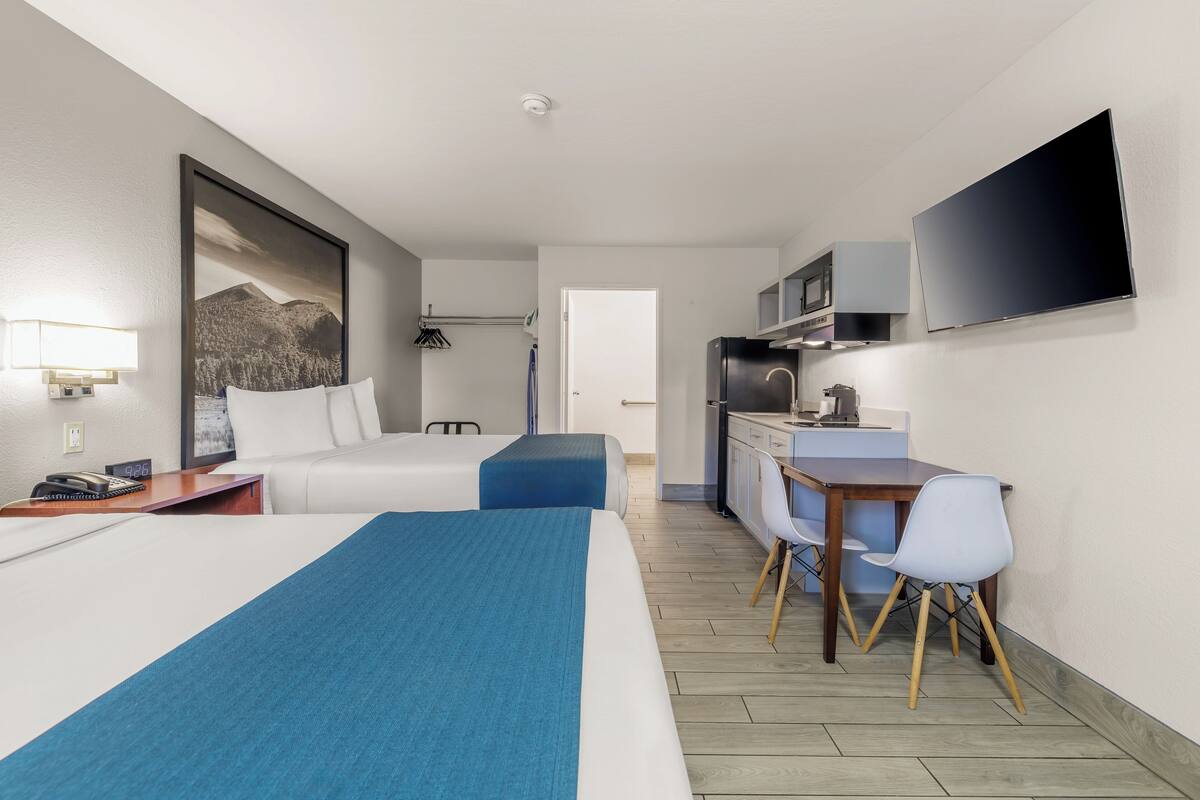 A hotel room with two beds, a desk with a chair, a microwave, a TV, and a small kitchenette.