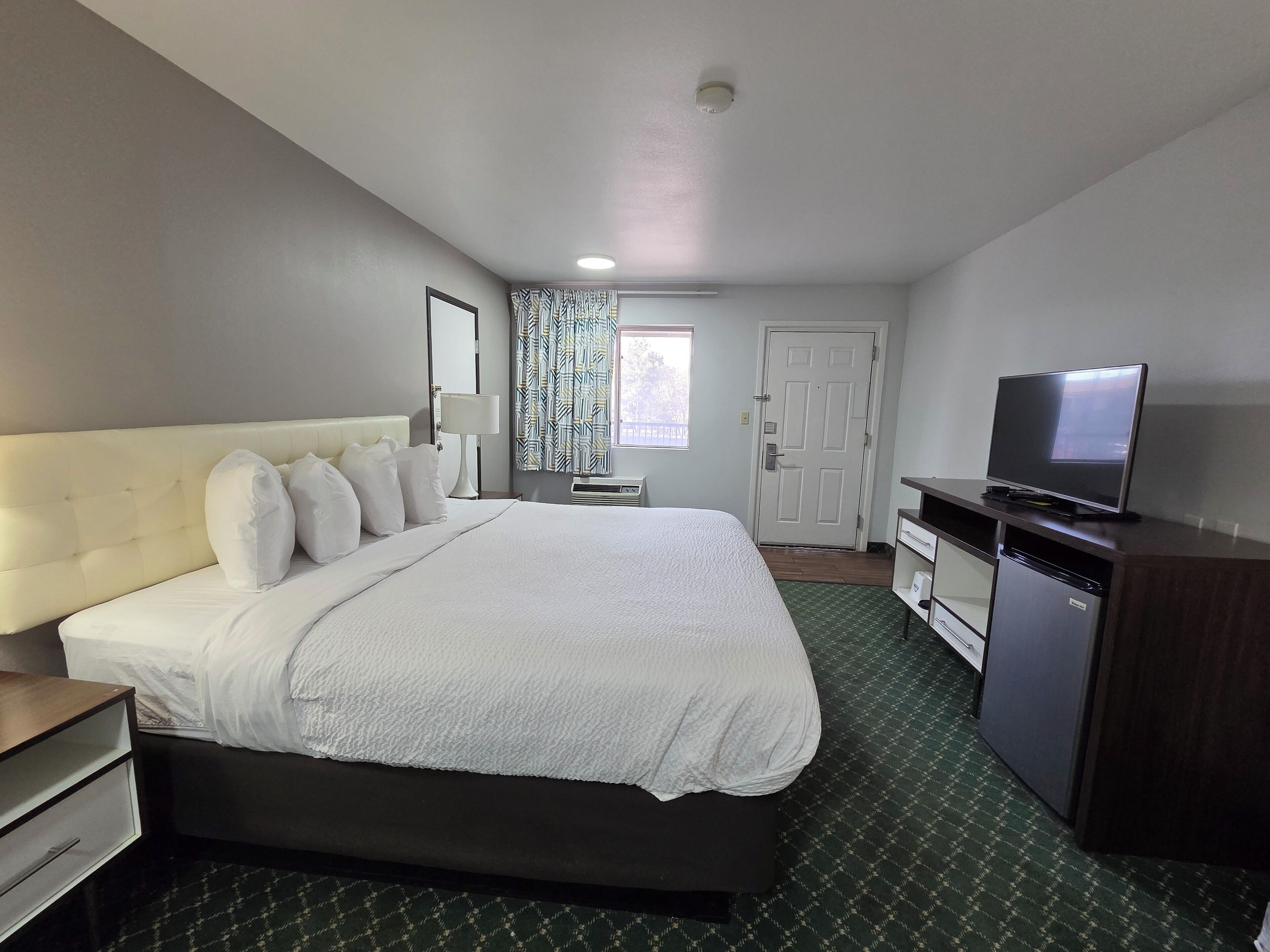 A hotel room with a large bed, a television, a desk, and a wardrobe.