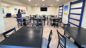 A dining area with multiple tables and chairs, a reception desk, and a TV mounted on the wall.