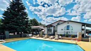 A swimming pool with lounge chairs, a covered seating area, and a building with a satellite dish.