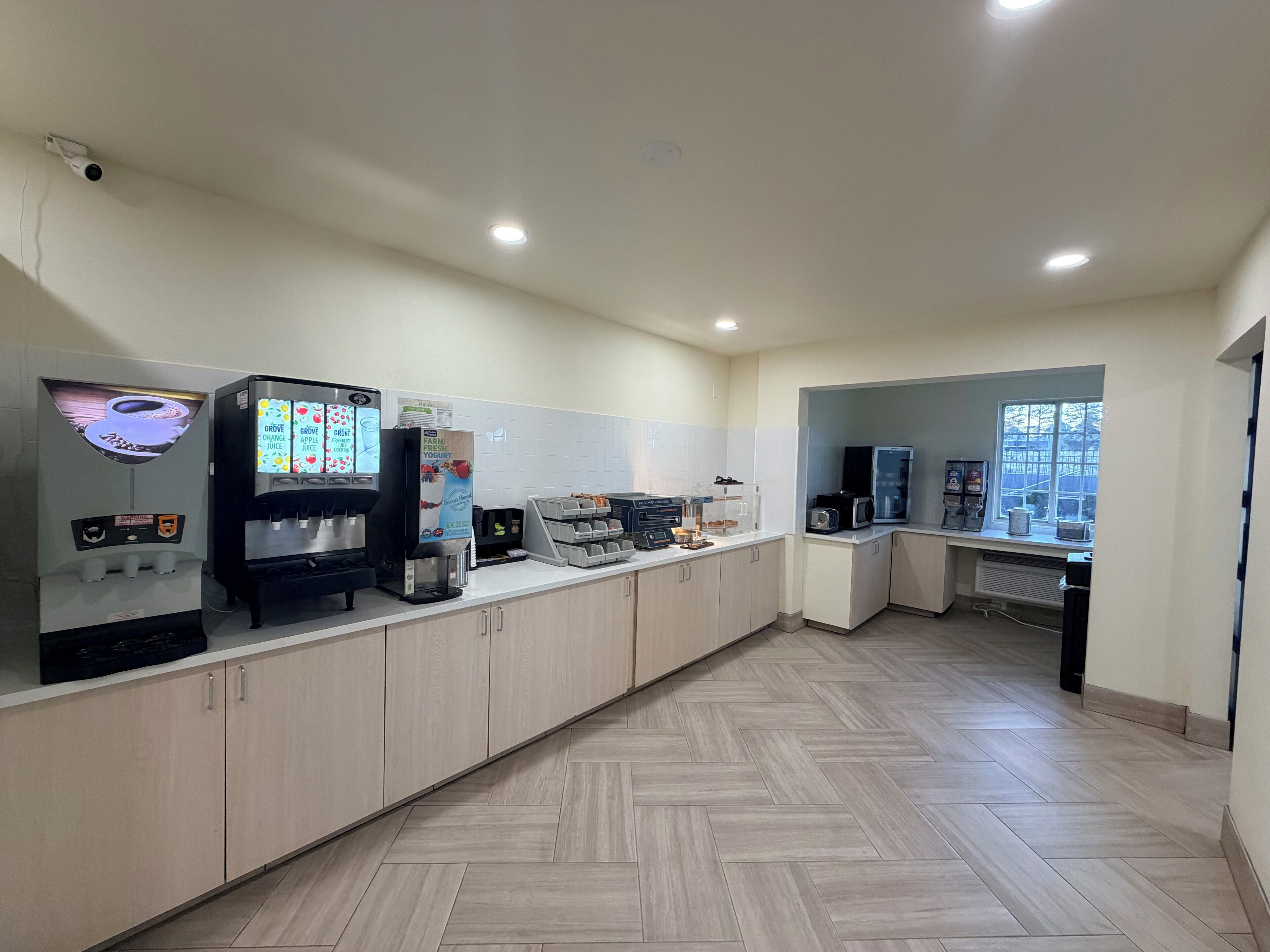 A clean, modern cafe with a long counter, a coffee machine, a juice dispenser, and a microwave.