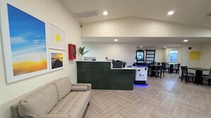 A hotel lobby with a reception desk, a sofa, a dining area, and artwork on the walls.