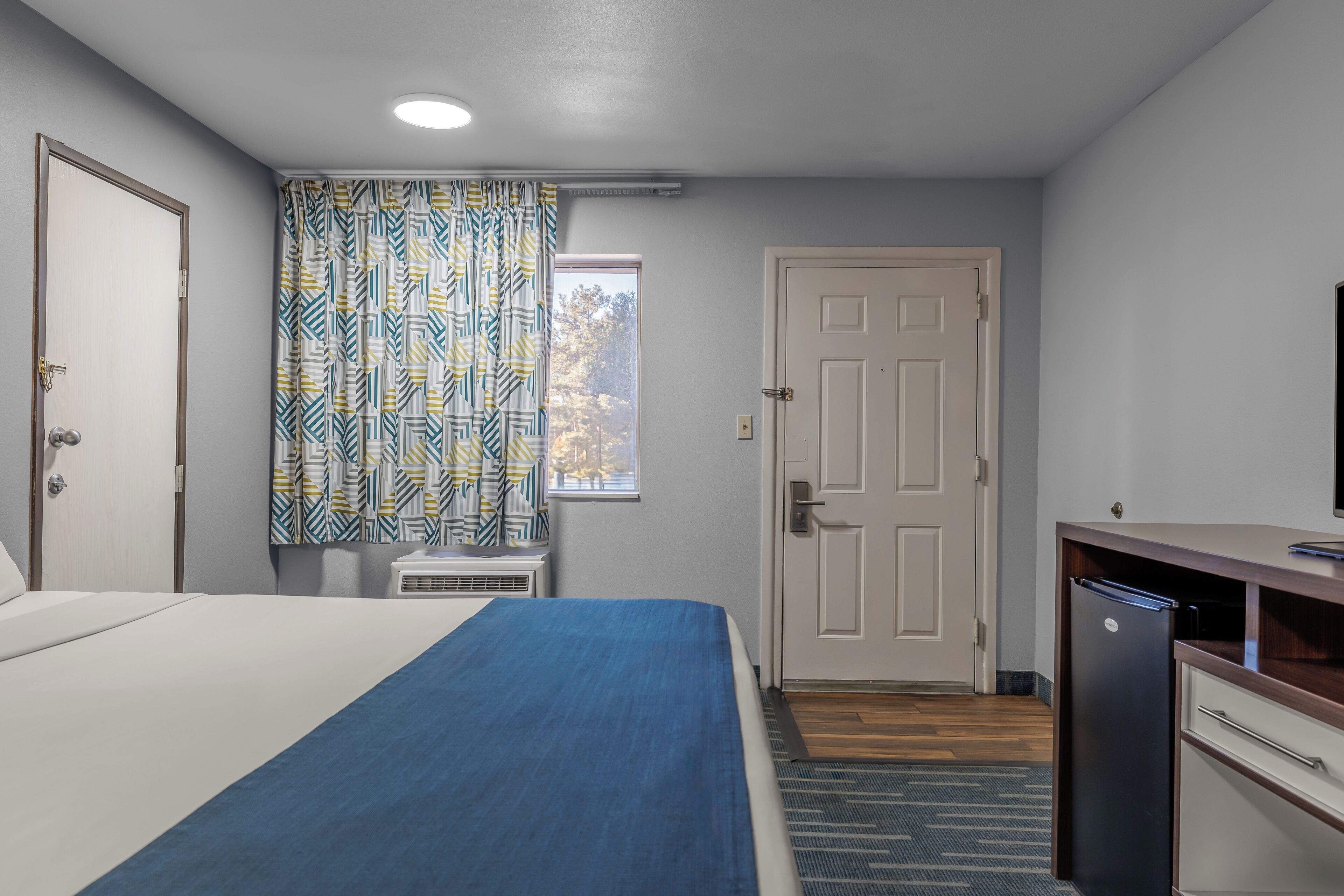 A hotel room with a bed, a desk, and a door.