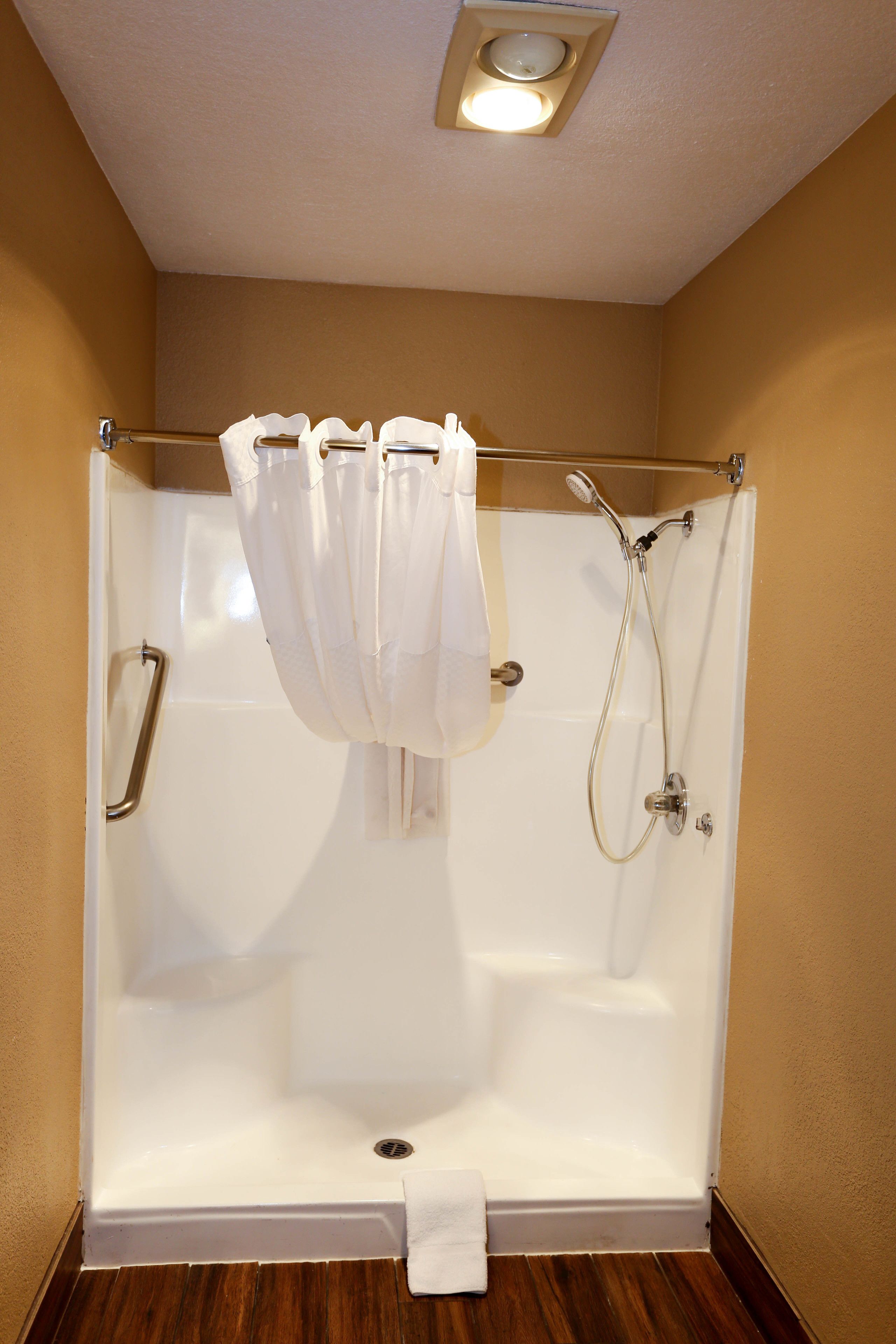 A shower with a white curtain, a handheld showerhead, and a handheld faucet.