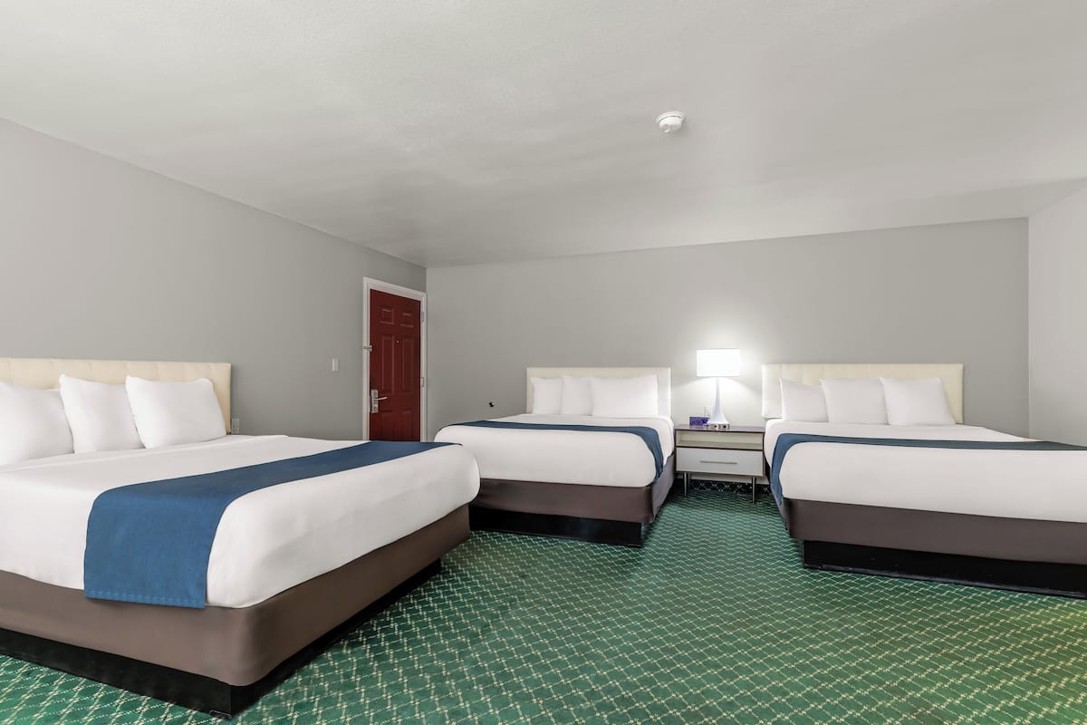 A hotel room with two beds, a desk, a chair, a lamp, and a door.