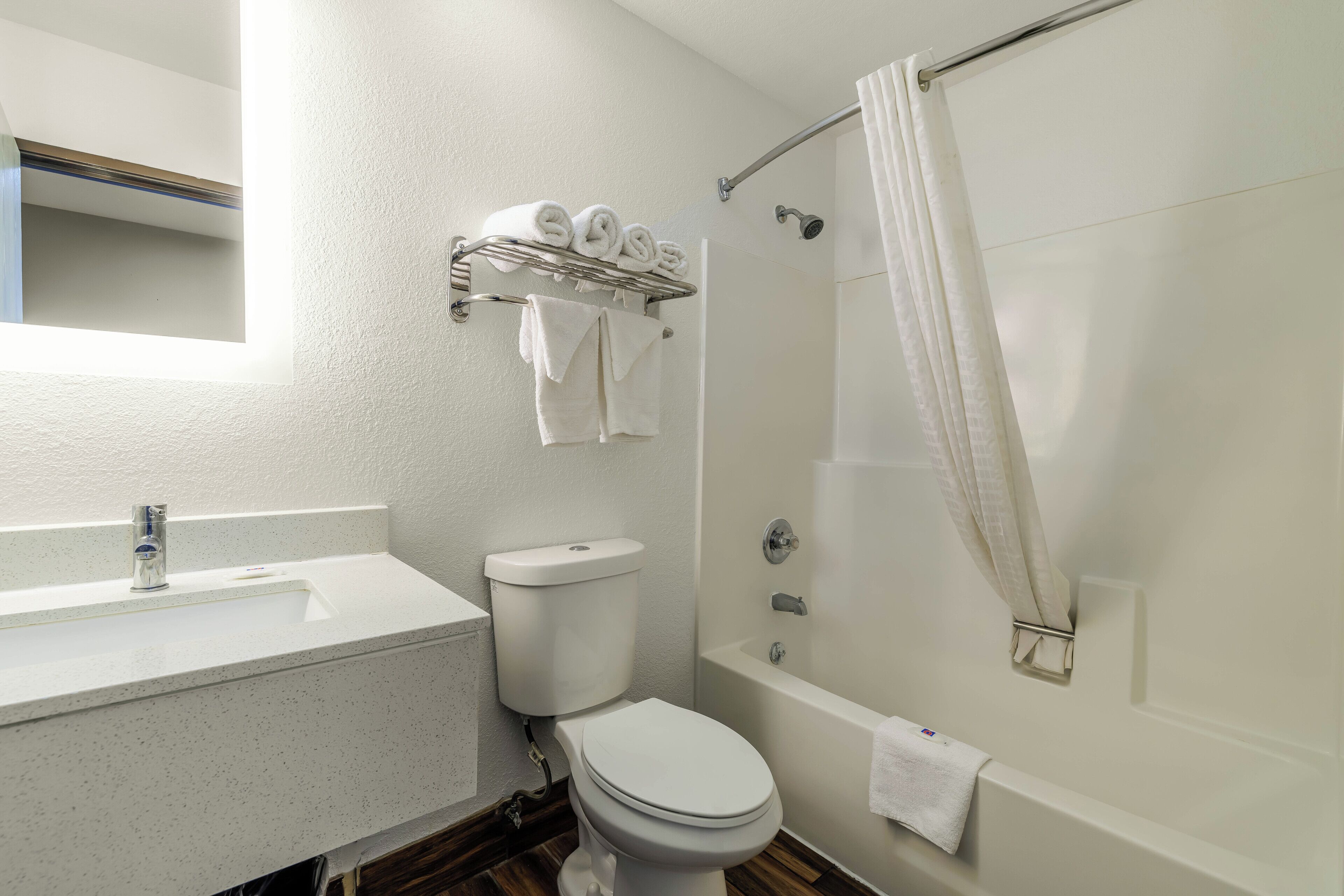 Une salle de bain avec un lavabo, des toilettes et une baignoire, tous de couleur blanche. On y trouve également un porte-serviettes avec des serviettes et un rideau de douche.
