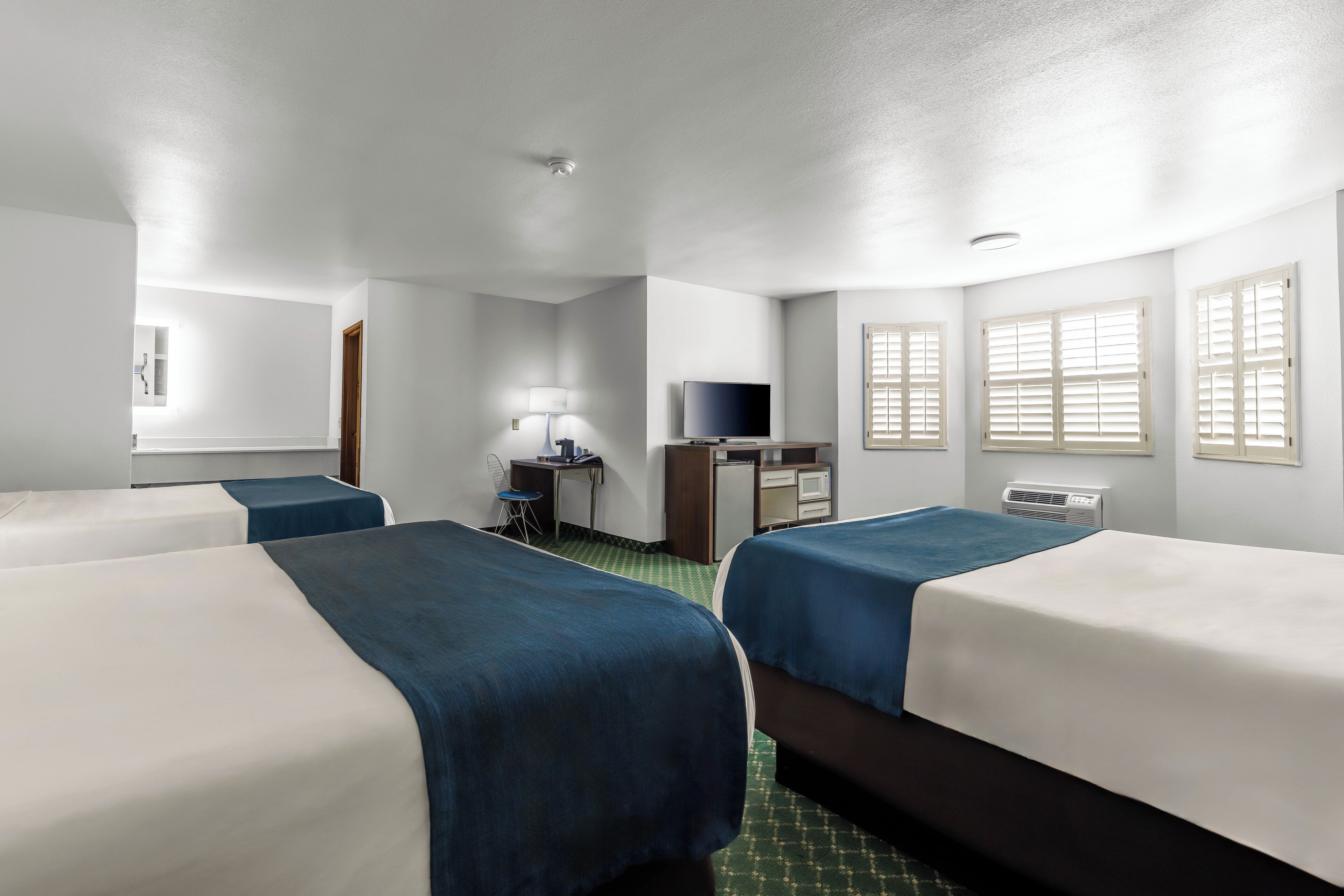 A hotel room with two beds, a desk, a television, and a window with blinds.