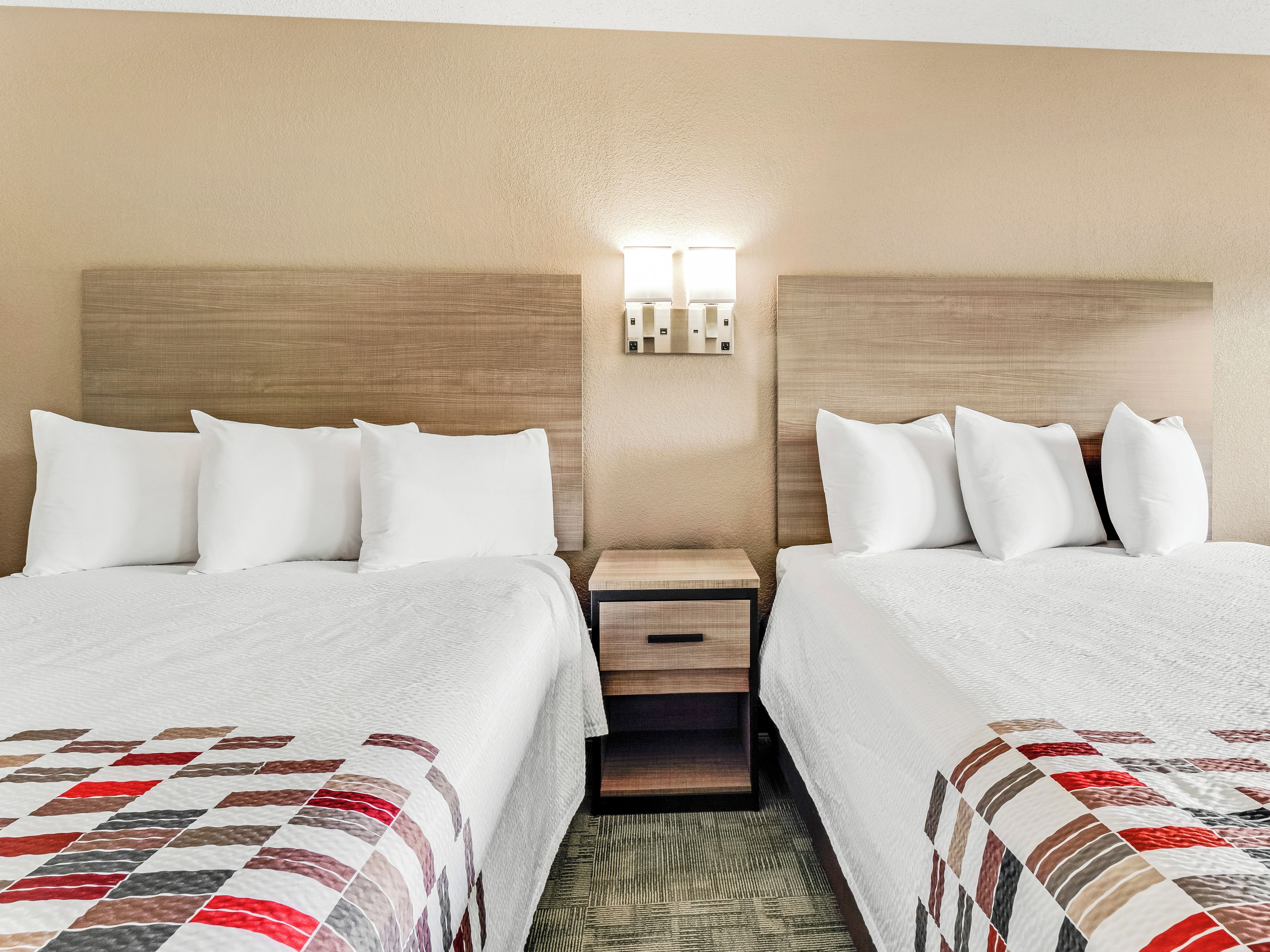 Une chambre d’hôtel avec deux lits, une table de chevet et un luminaire fixé au mur.