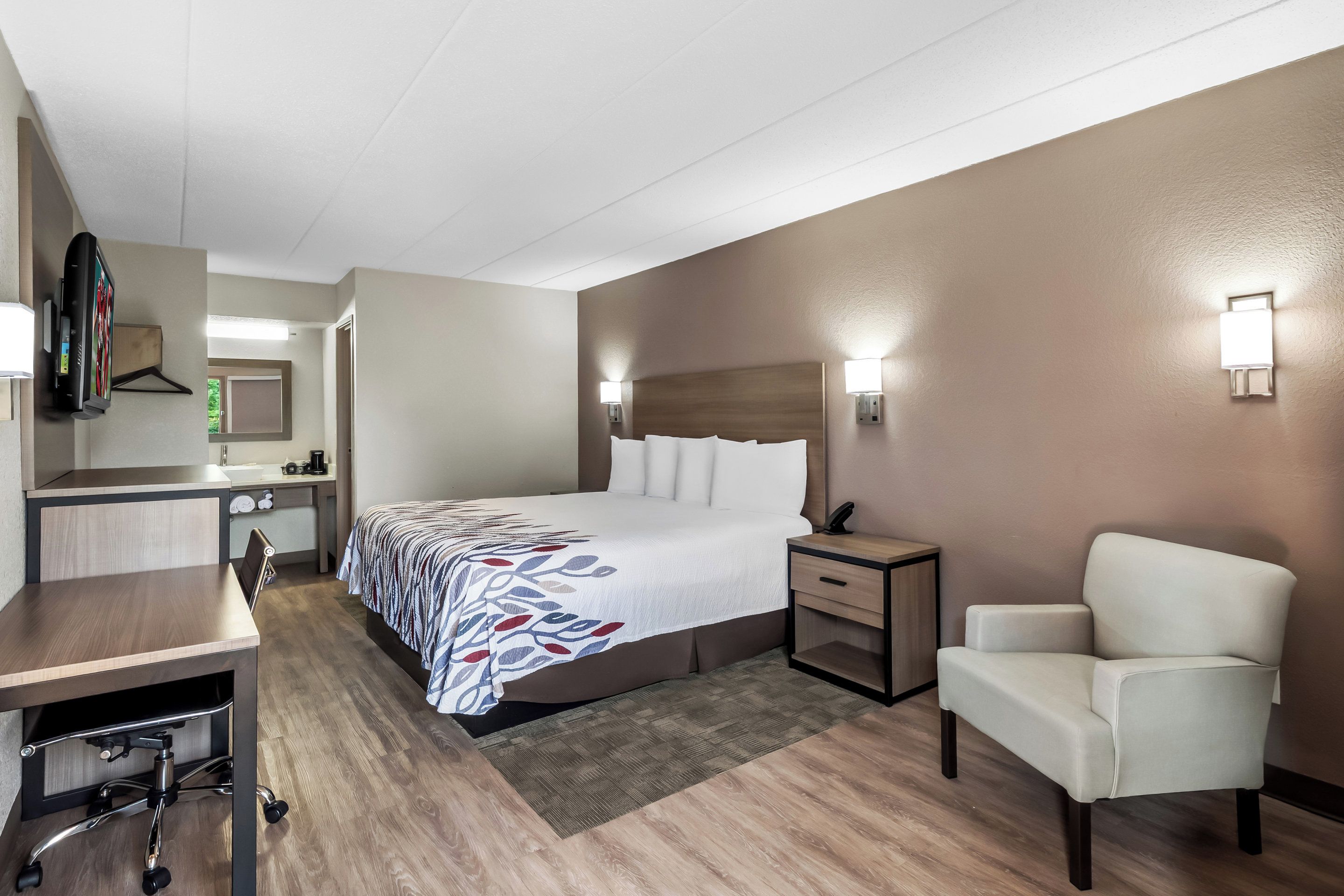 Une chambre d’hôtel comprenant un lit, une table de chevet, une chaise, un bureau et un miroir.