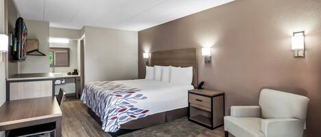 Una habitación de hotel con cama, mesita de noche, silla, escritorio y espejo.