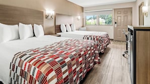 Habitación de hotel con dos camas, un escritorio, un espejo y una ventana con vistas al exterior.