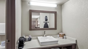 Un baño con un lavamanos blanco, un espejo, una cafetera y un perchero para toallas.