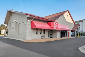 Un Red Roof Inn con toldo rojo, fachada de ladrillo y cielo despejado.