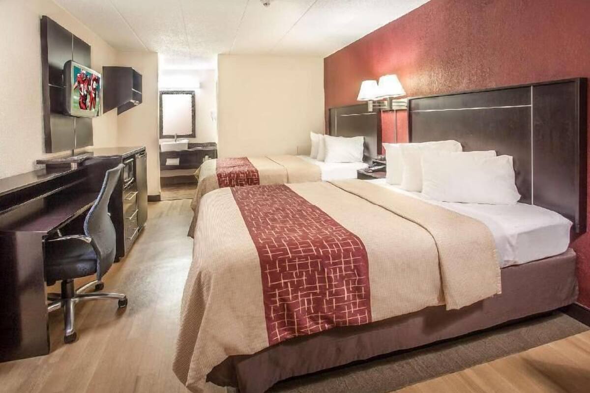 A hotel room with two beds, a desk, a chair, a TV, and a lamp.