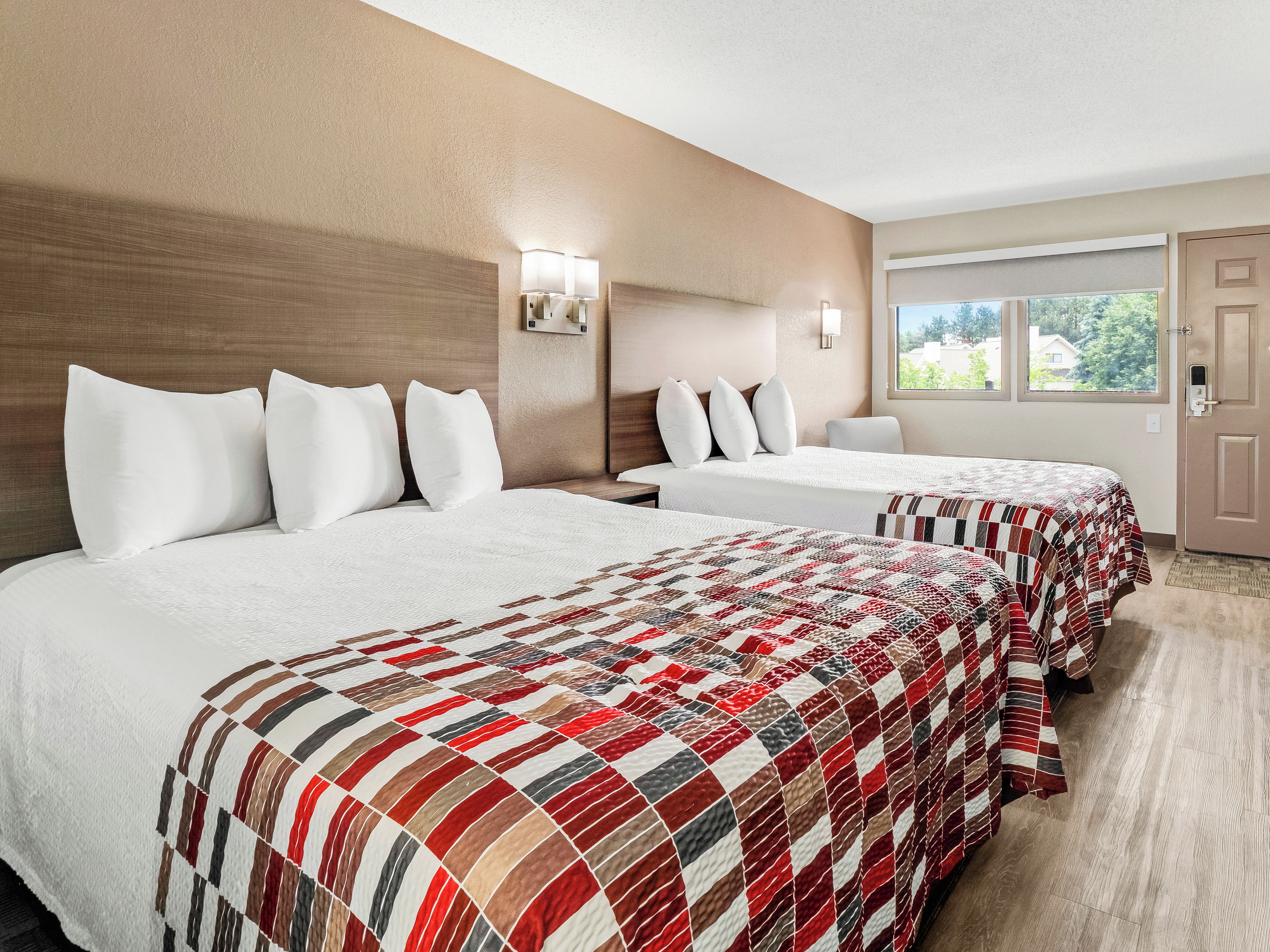 A hotel room with two beds, a large window, and a door.
