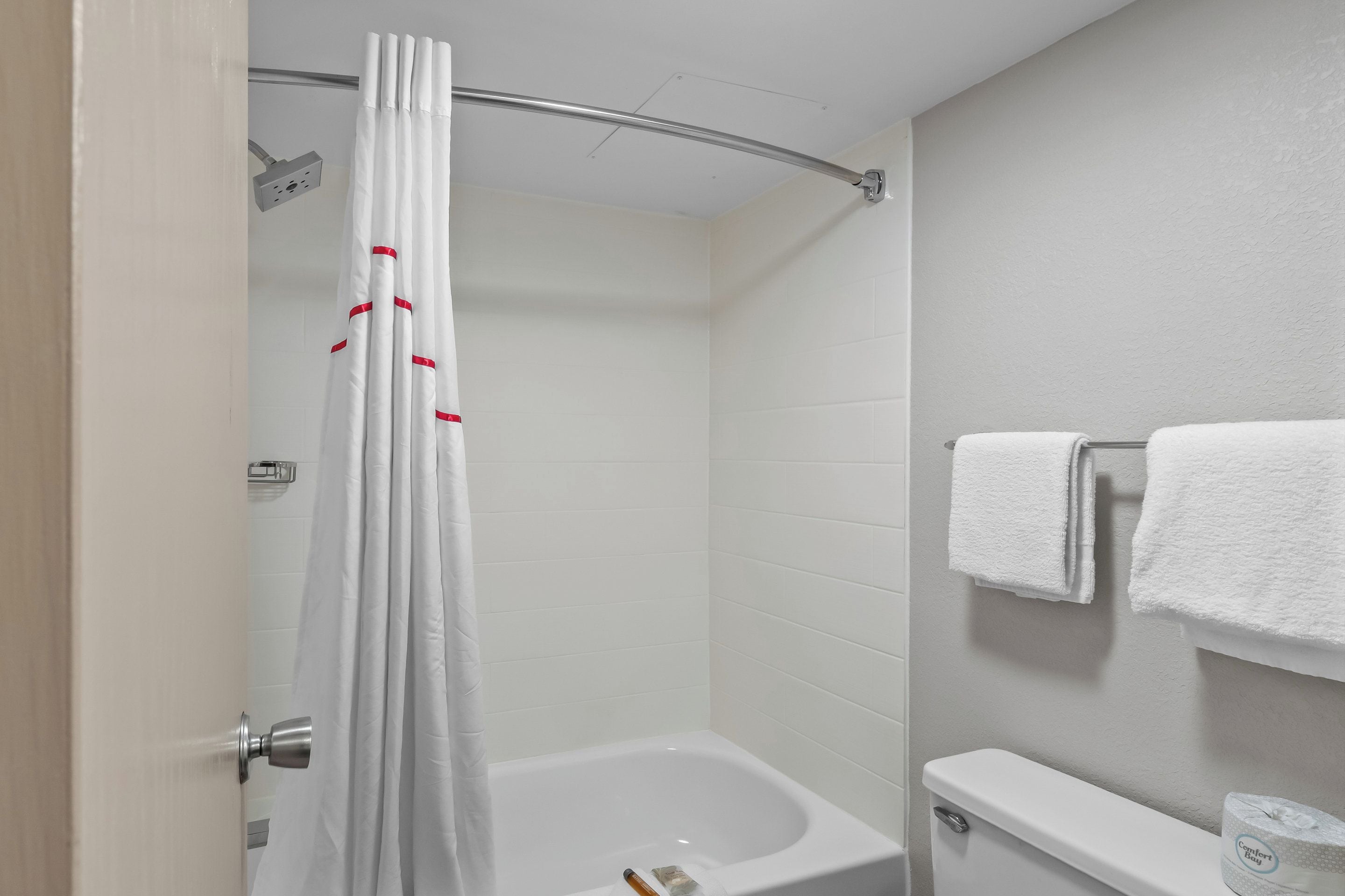 A bathroom with a shower curtain, a bathtub, a toilet, and a towel rack with towels.