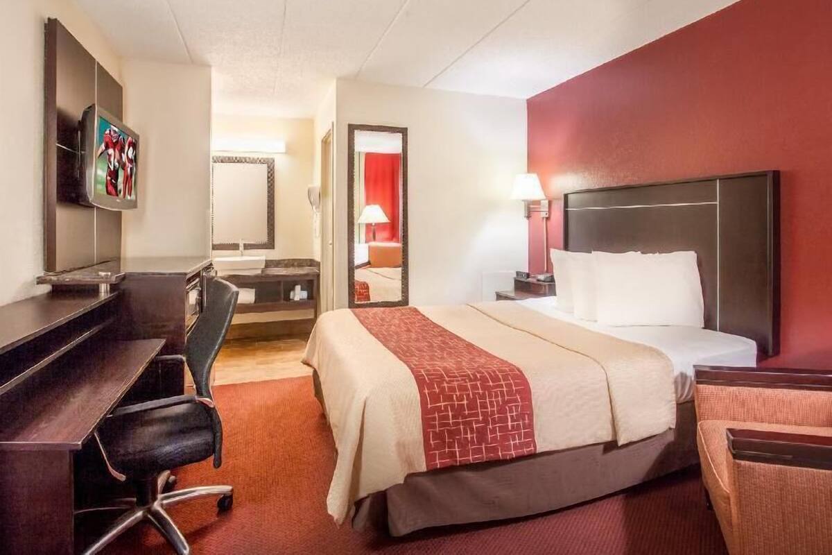 A hotel room with a bed, desk, chair, TV, and a mirror.