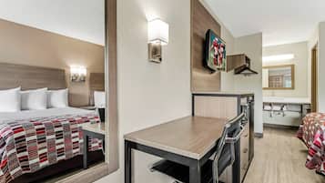 Una habitación de hotel con cama, escritorio, silla, espejo, televisor y baño.