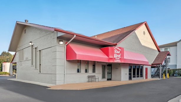 Un Red Roof Inn con toldo rojo, fachada de ladrillo y cielo despejado.