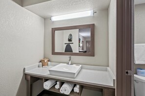 Un baño con un lavamanos blanco, un espejo y un perchero para toallas.