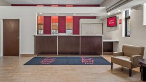 Zona de recepción de hotel con un mostrador, una silla y una pantalla digital que muestra 'Wi-Fi gratis en todas las habitaciones'.