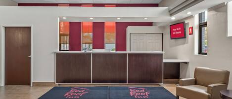A hotel reception area with a desk, a chair, and a digital screen displaying 'Free Wi-Fi All Rooms'.