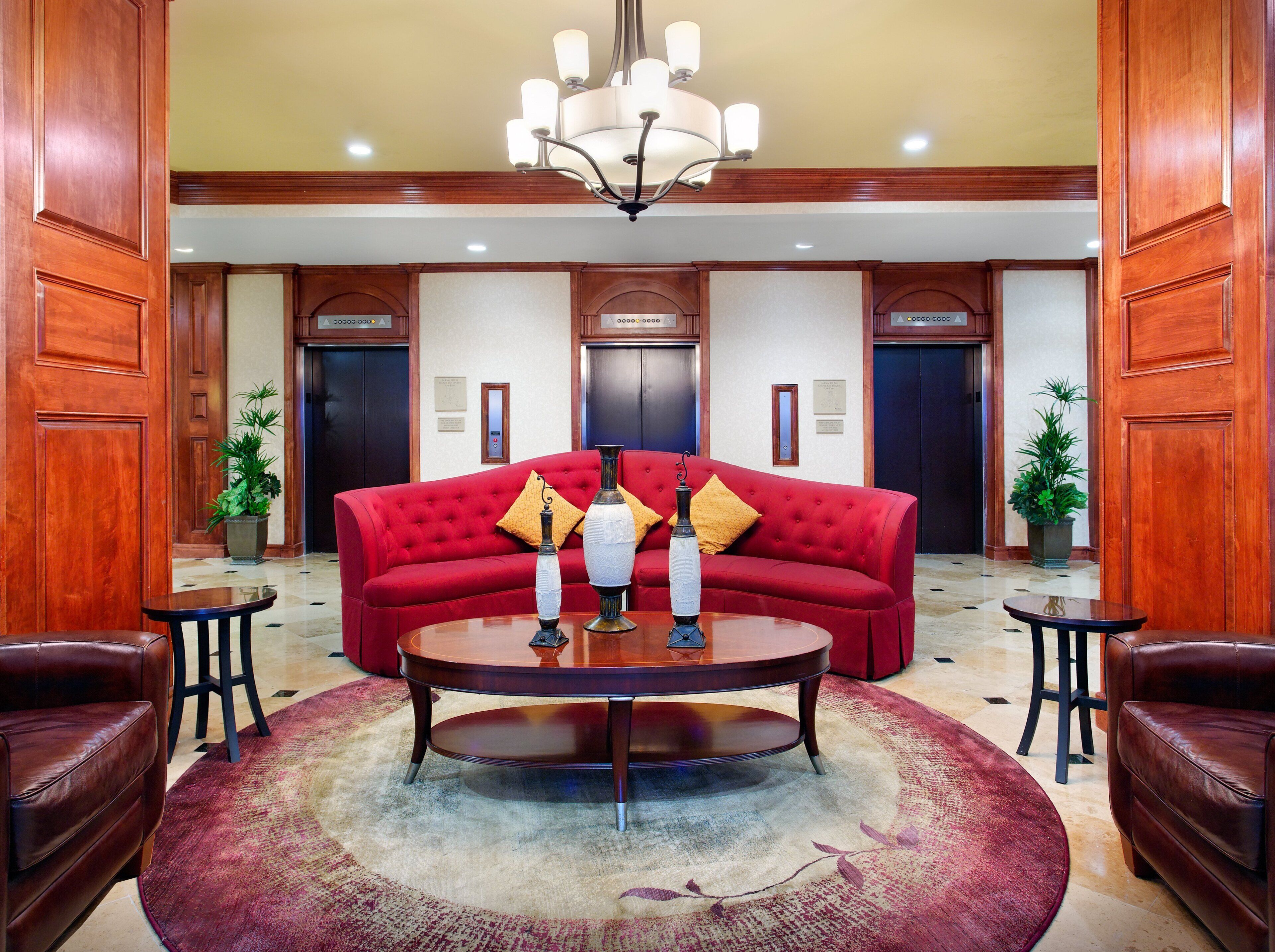 A lobby with a red sofa, a round table, and two potted plants.