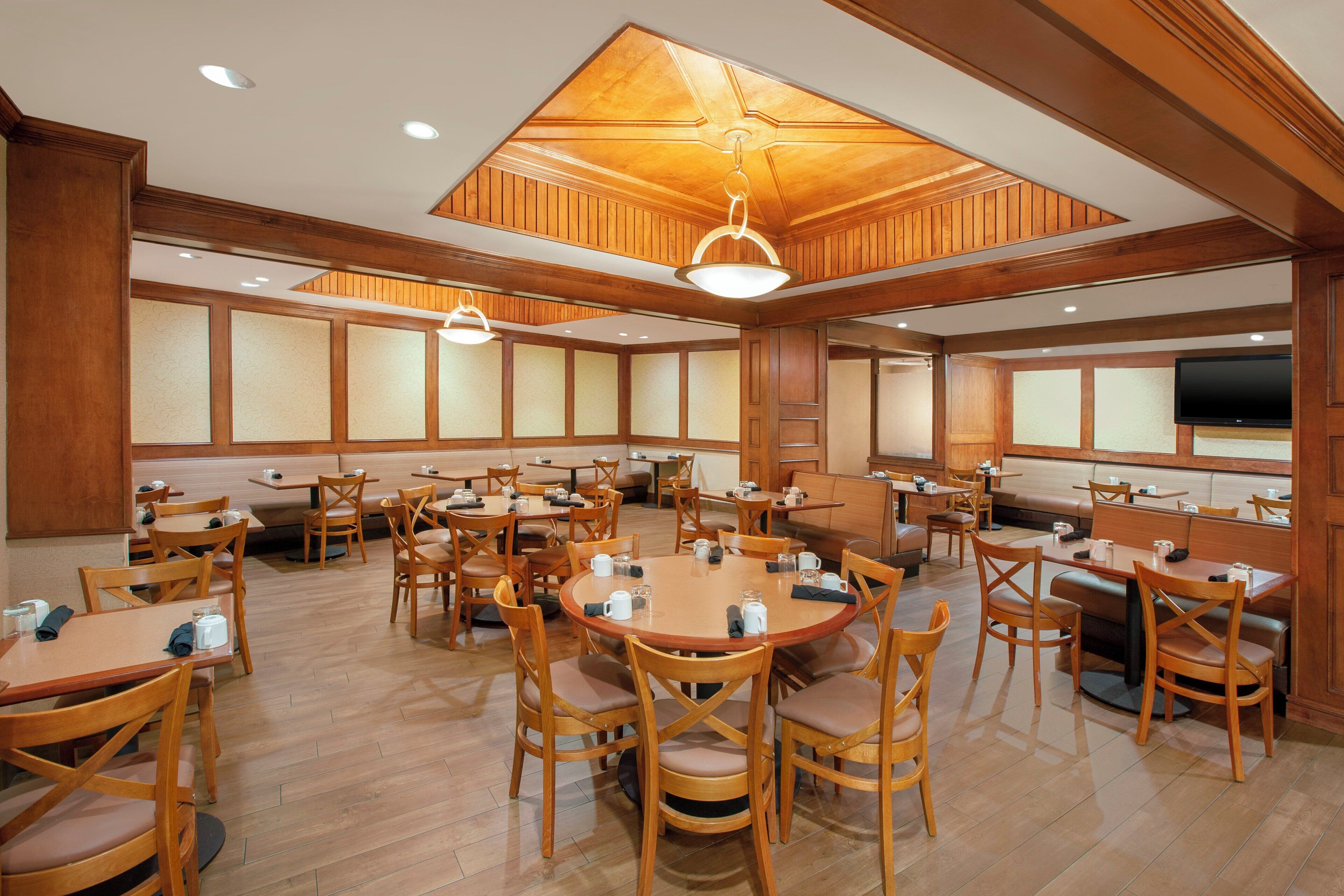 A spacious dining area with multiple tables and chairs, wooden paneling on the walls, and a ceiling with recessed lighting.