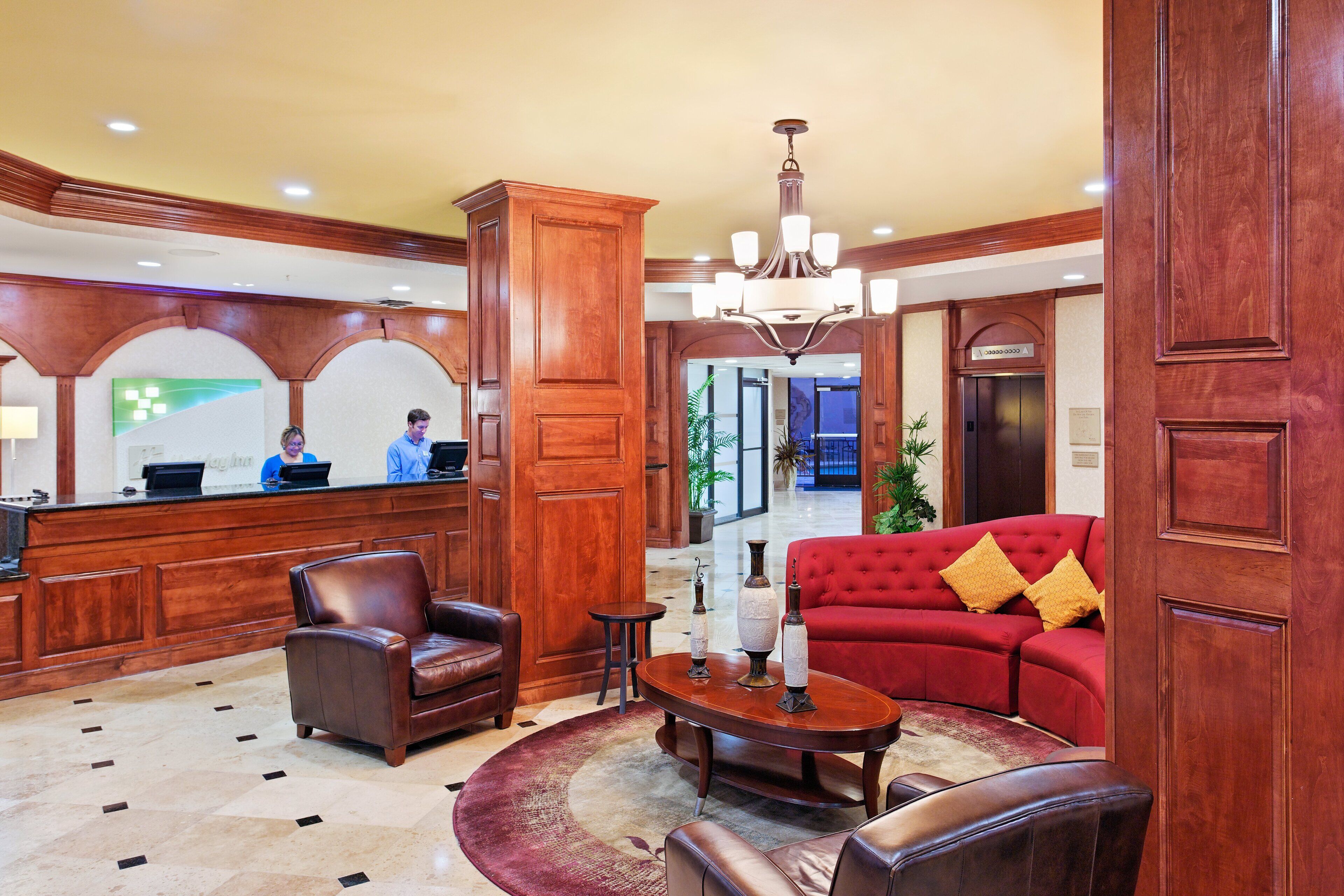 A lobby with a reception desk, a red sofa, leather chairs, a chandelier, and a patterned rug.