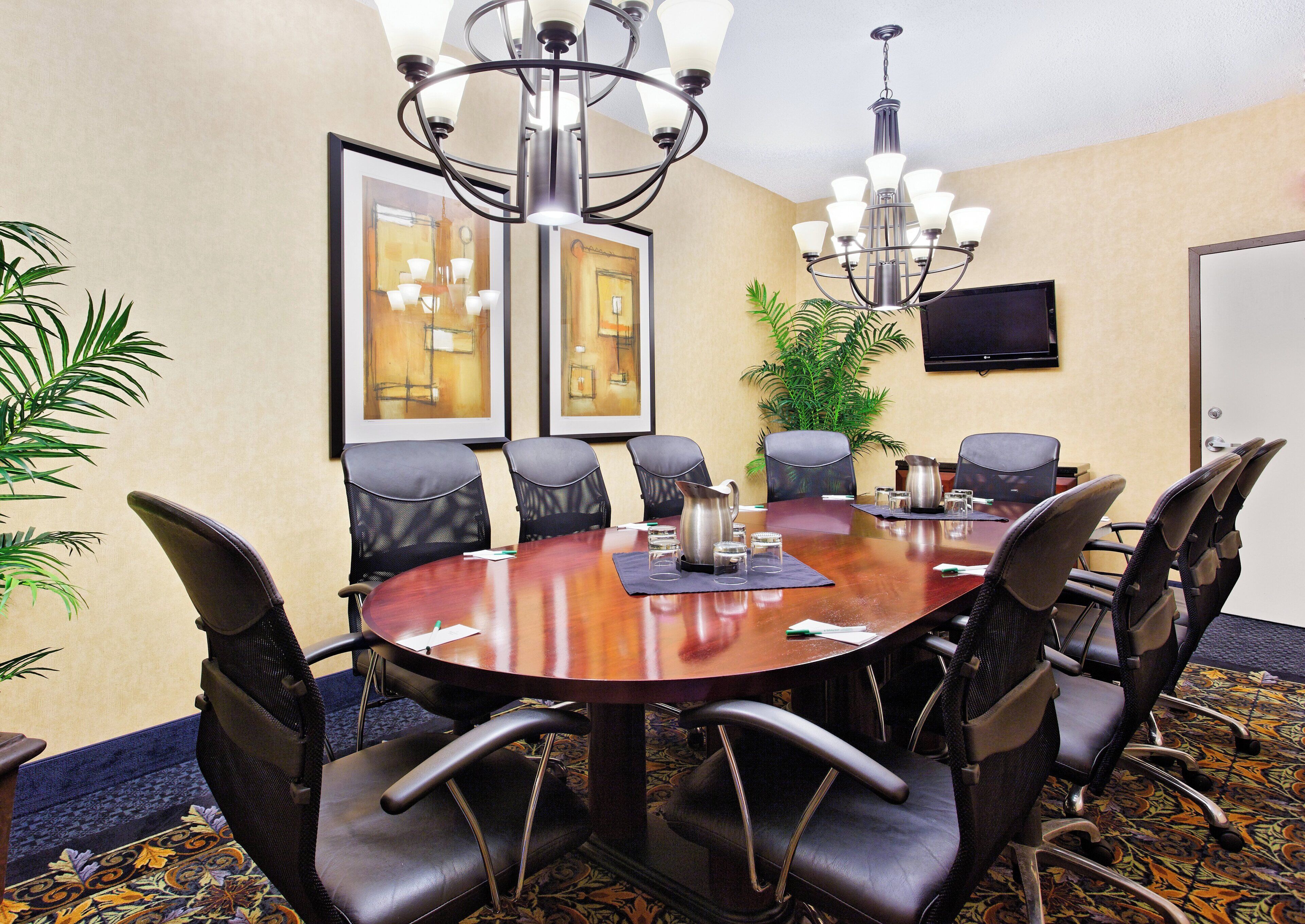 A conference room with a round table, chairs, a chandelier, artwork on the walls, and a television.