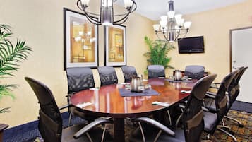 A conference room with a round table, chairs, a chandelier, artwork on the walls, and a television.
