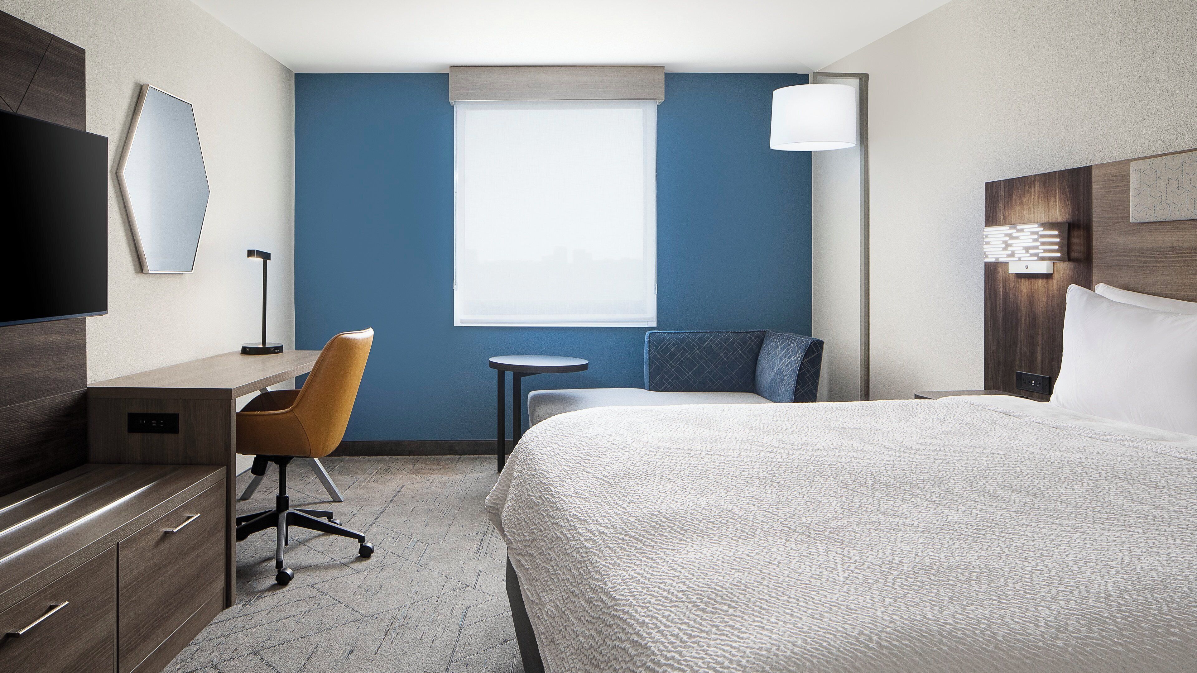 Une chambre d’hôtel avec un lit, un bureau, une chaise, une petite table et une fenêtre.